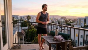 calm man standing on balcony after morning workout, sunrise in background – alt text: "Man practicing mindfulness after fitness session for mental health