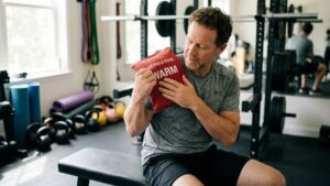 A person applying a warm gel pack to their shoulder before exercise